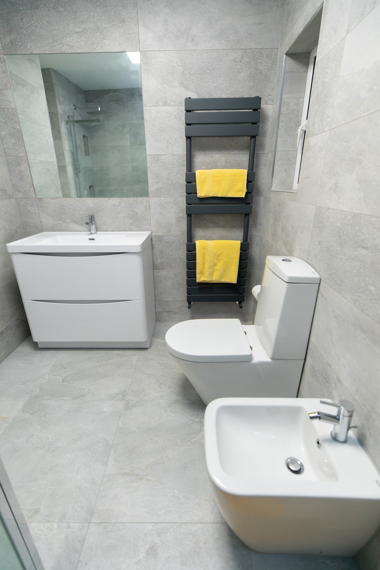 Modern grey-tile bathroom with wall-hung vanity, anthracite towel rail and contemporary WC — bathroom fitting by RJS Innovative Building, East London