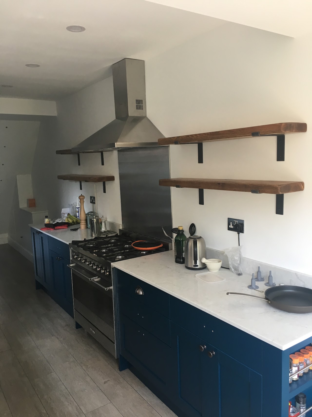 Navy shaker kitchen with stainless extractor canopy and reclaimed timber shelving — kitchen fitting by RJS Innovative Building, East London