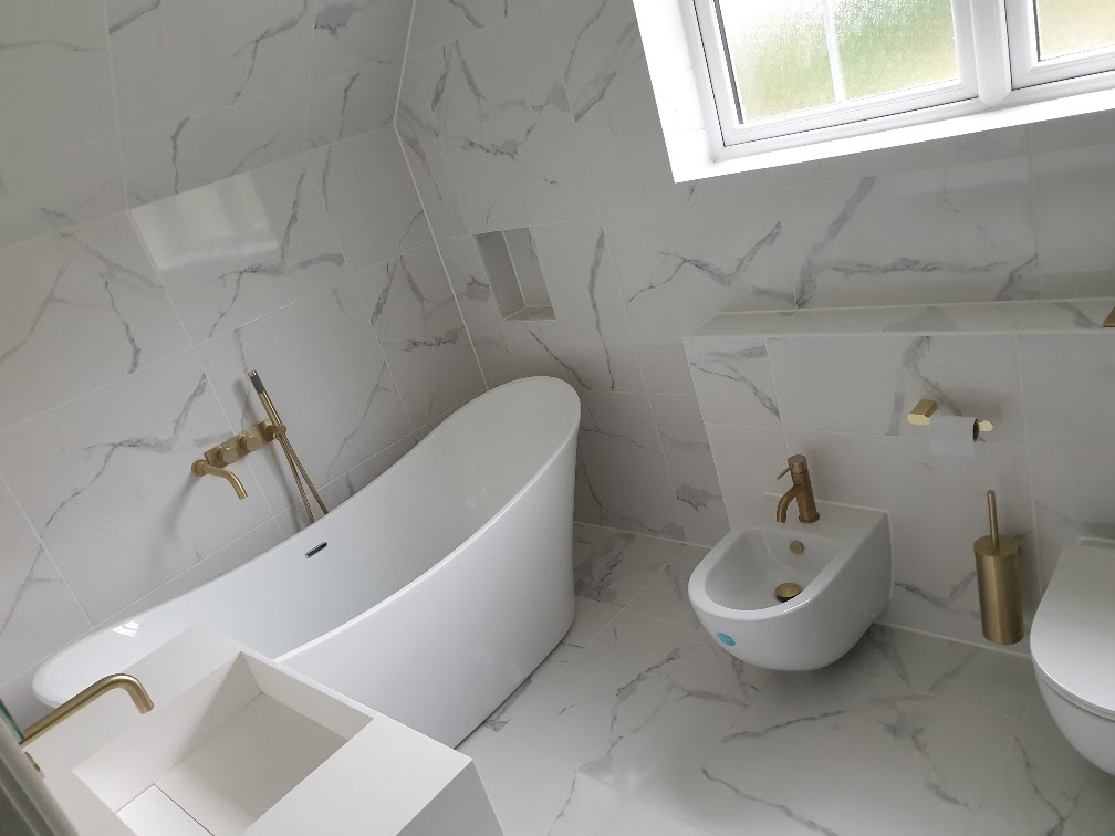Freestanding bath with brushed-gold wall mixer and marble-effect tiling — bathroom refurbishment by RJS Innovative Building, East London