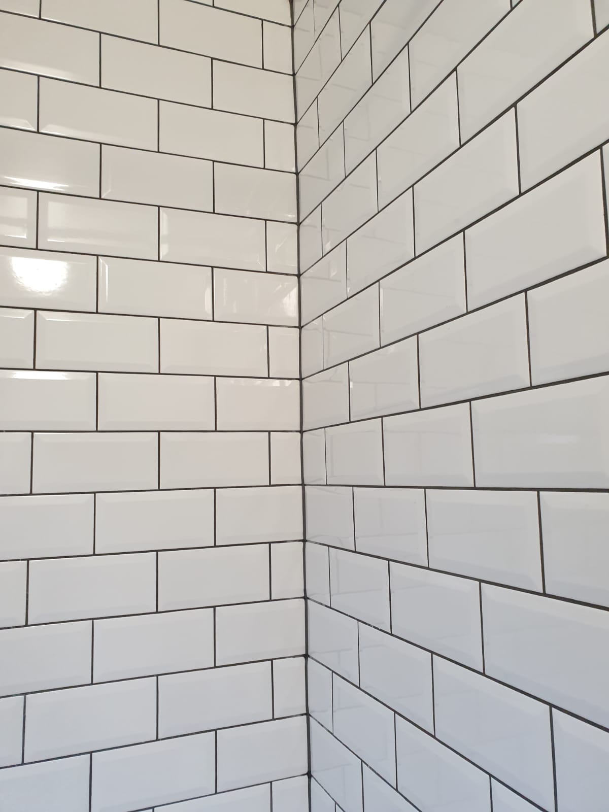 White metro subway tiling with dark grout in a corner shower wall — tiling by RJS Innovative Building, East London