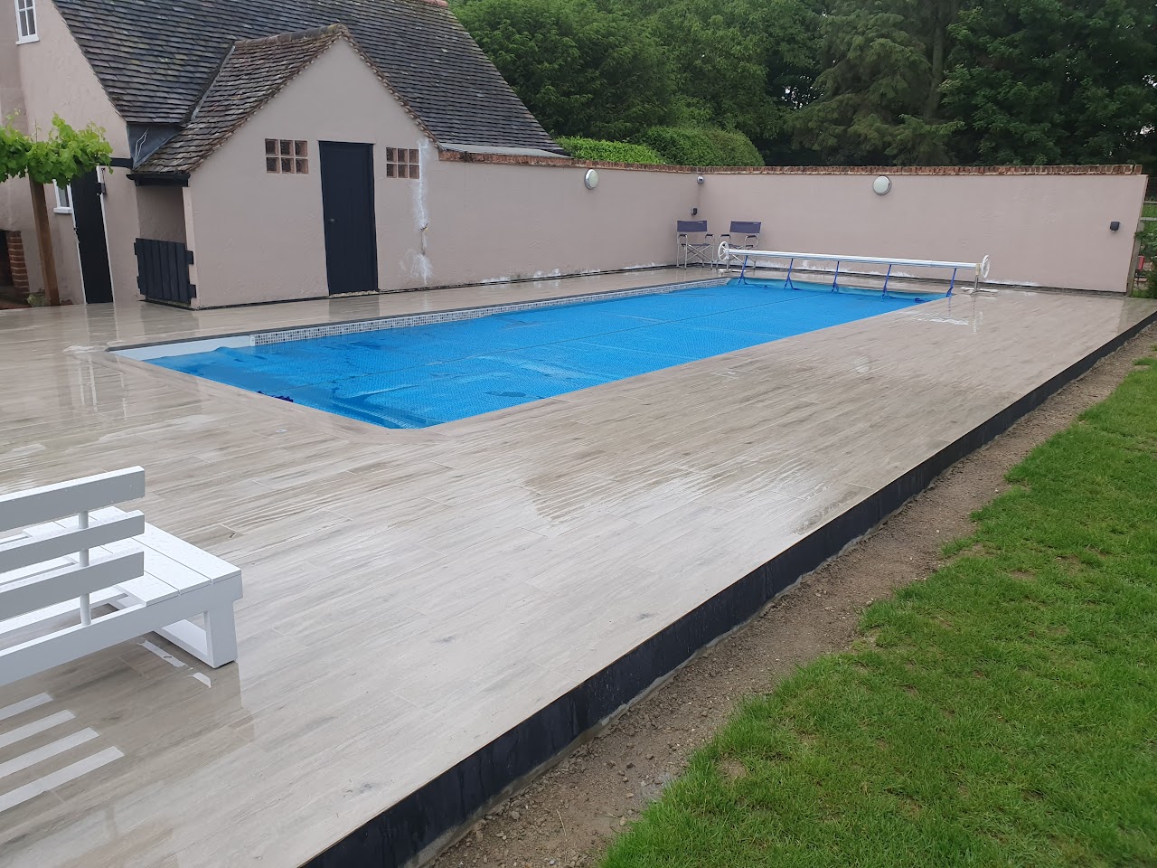Outdoor swimming pool with timber-look porcelain surround and white sun loungers — swimming pool construction by RJS Innovative Building, East London